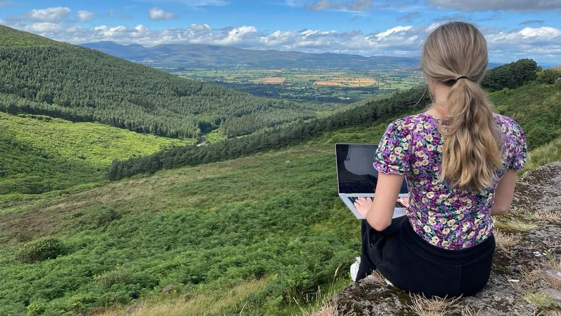Yvonne Murphy sitting with her laptop computer looking over the Irish landscape.