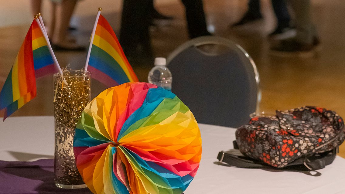 Rainbow-colored paper decoration, rainbow flags and small purse on table at party