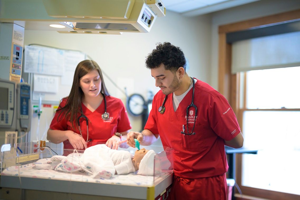 Nursing students participate in a nursing simulation - taking care of an infant manikin in a hospital bassinet.