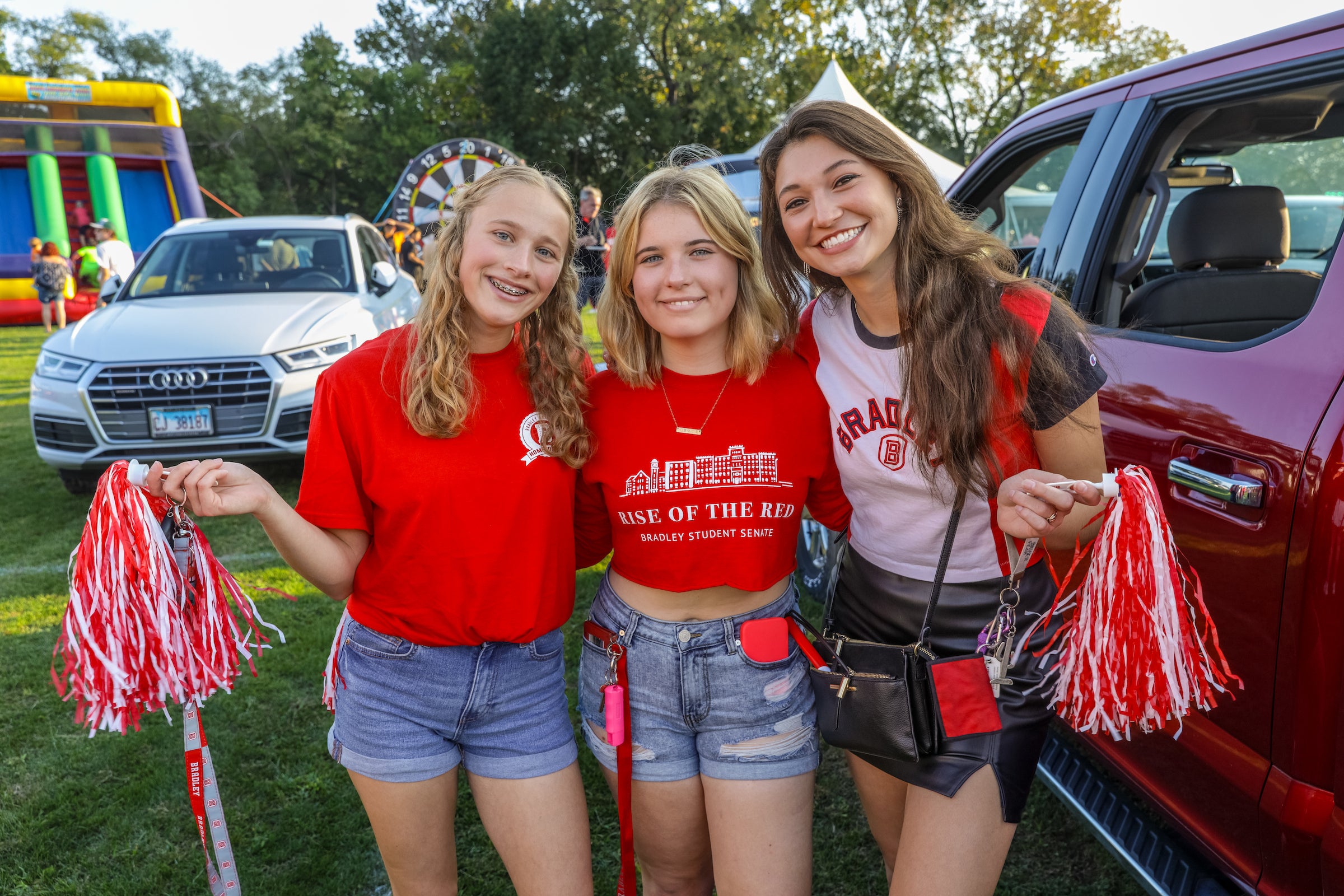 Three female students smiling and posing for a photo with pom-poms