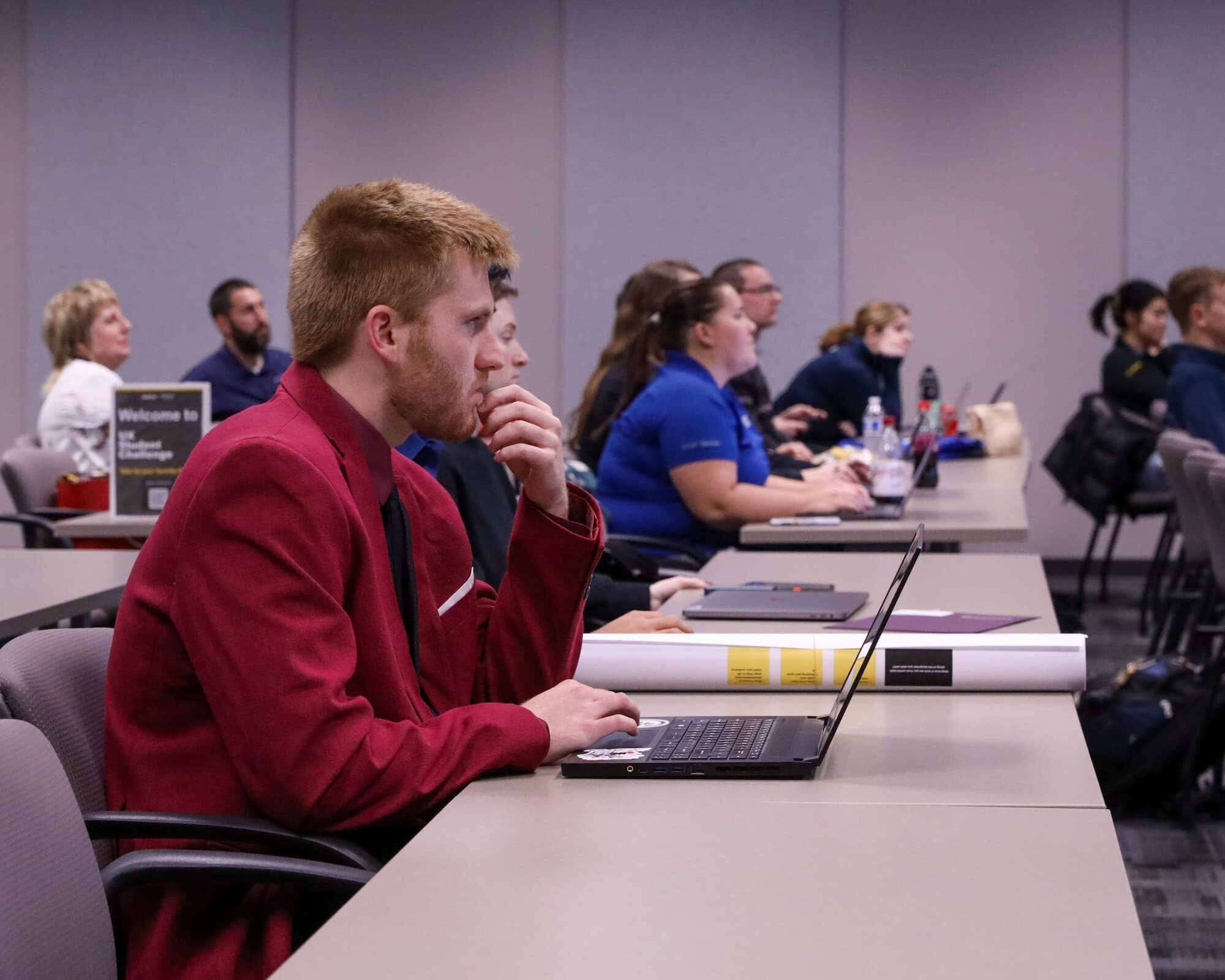 Students sitting in a classroom with laptops open listening to a professor out of frame