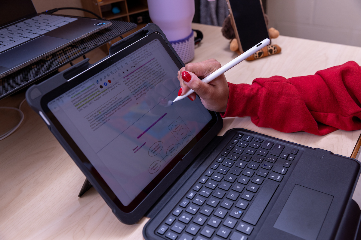 A hand taking notes on a touch screen laptop