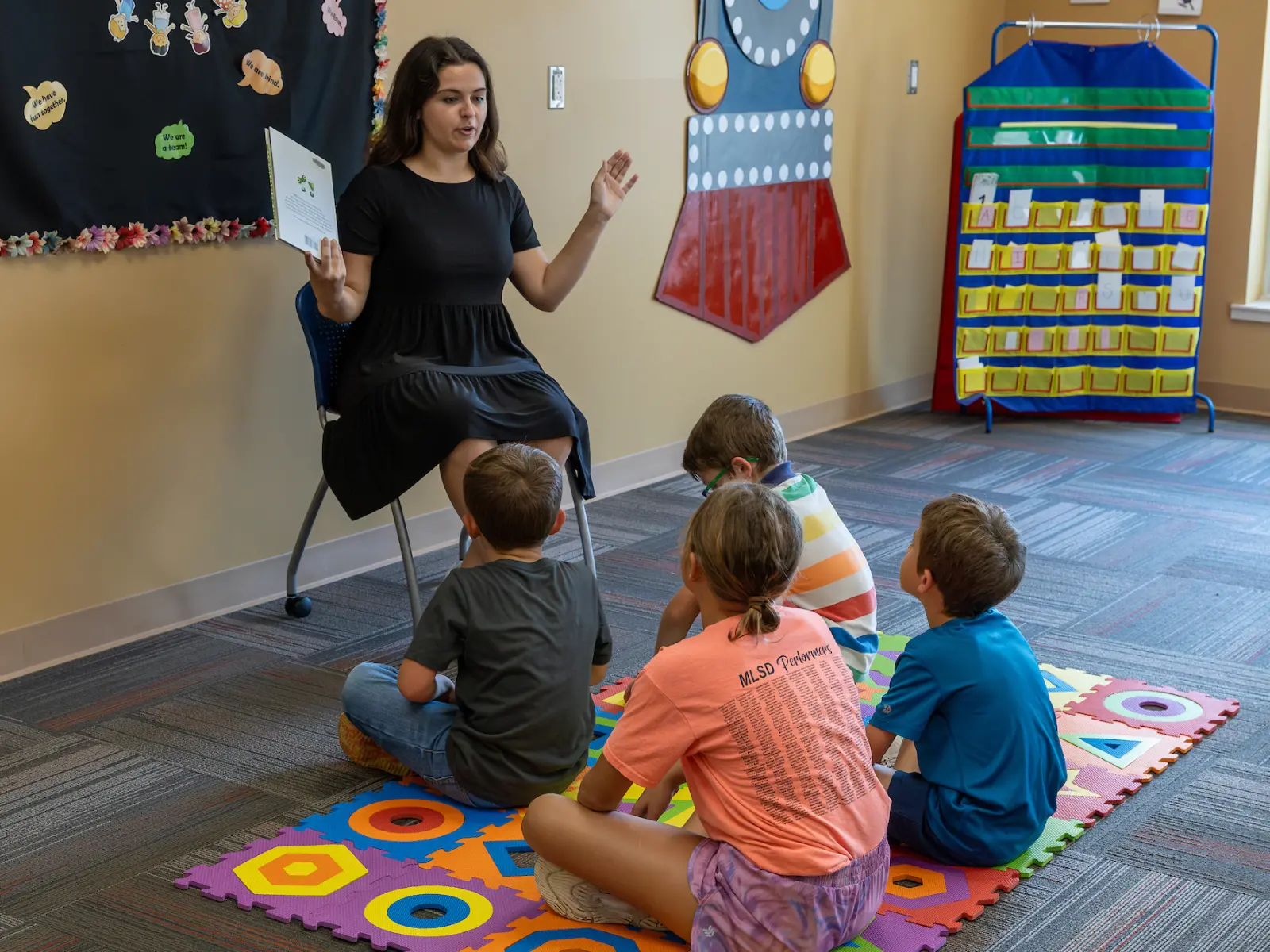 A female teacher sitting down instructing some elementary age students