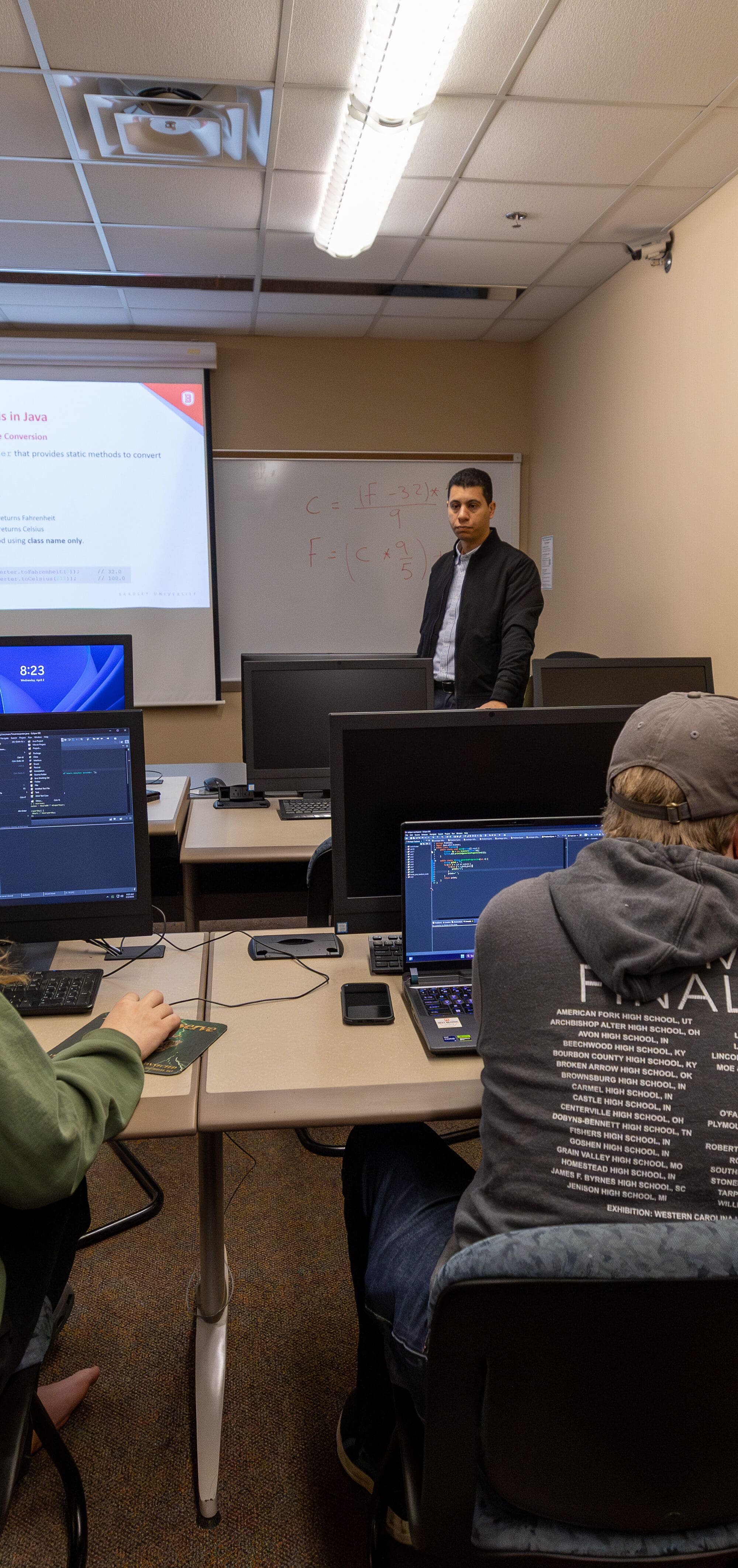 Students in a class room with laptops listening to a professor