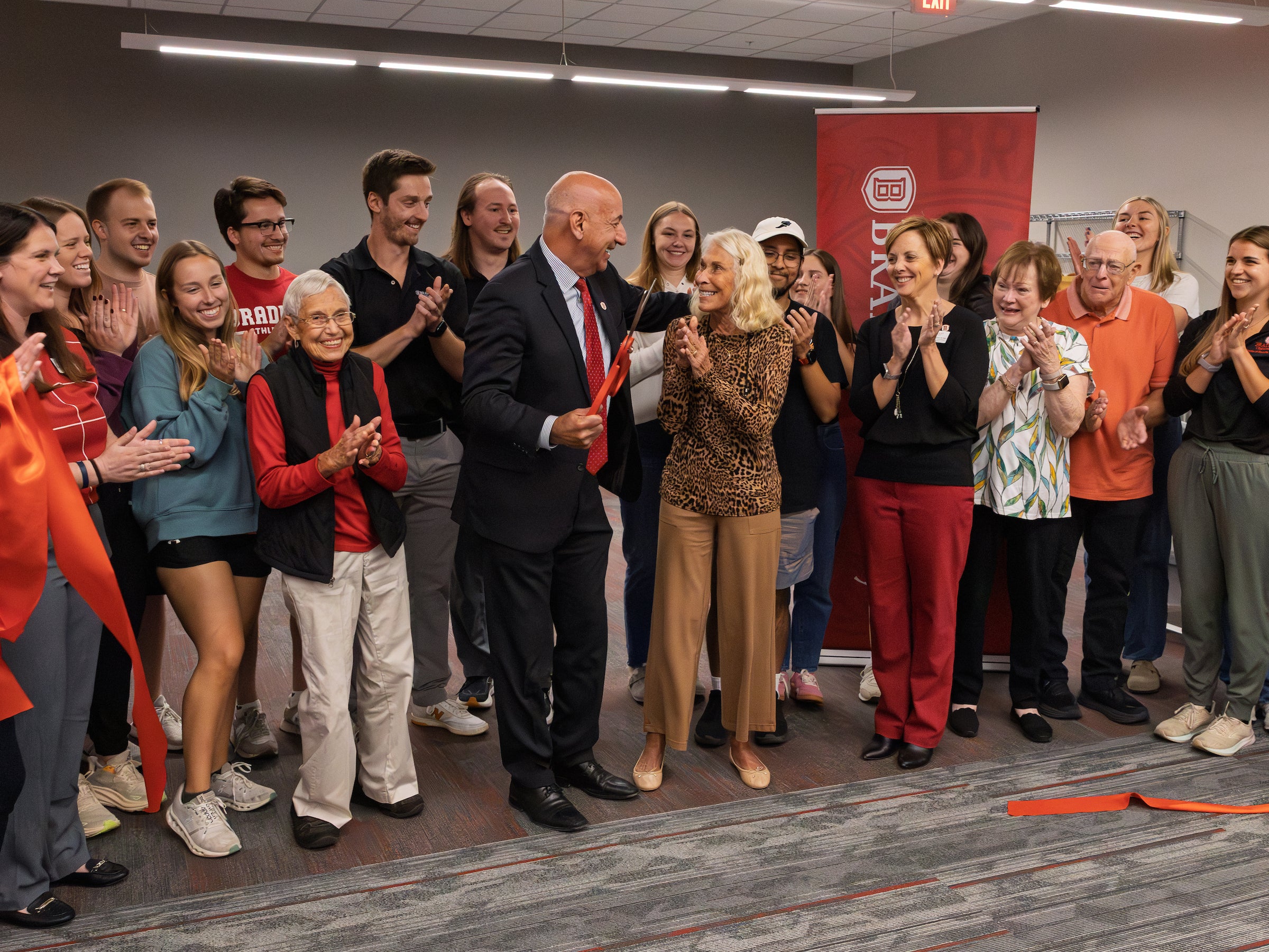 A crowd of people celebrating inside the clinic behind a red ribbon that has just been cut.