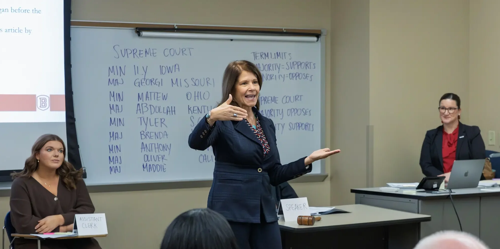 A professor speaking to a class with political terminology on a whiteboard in the background