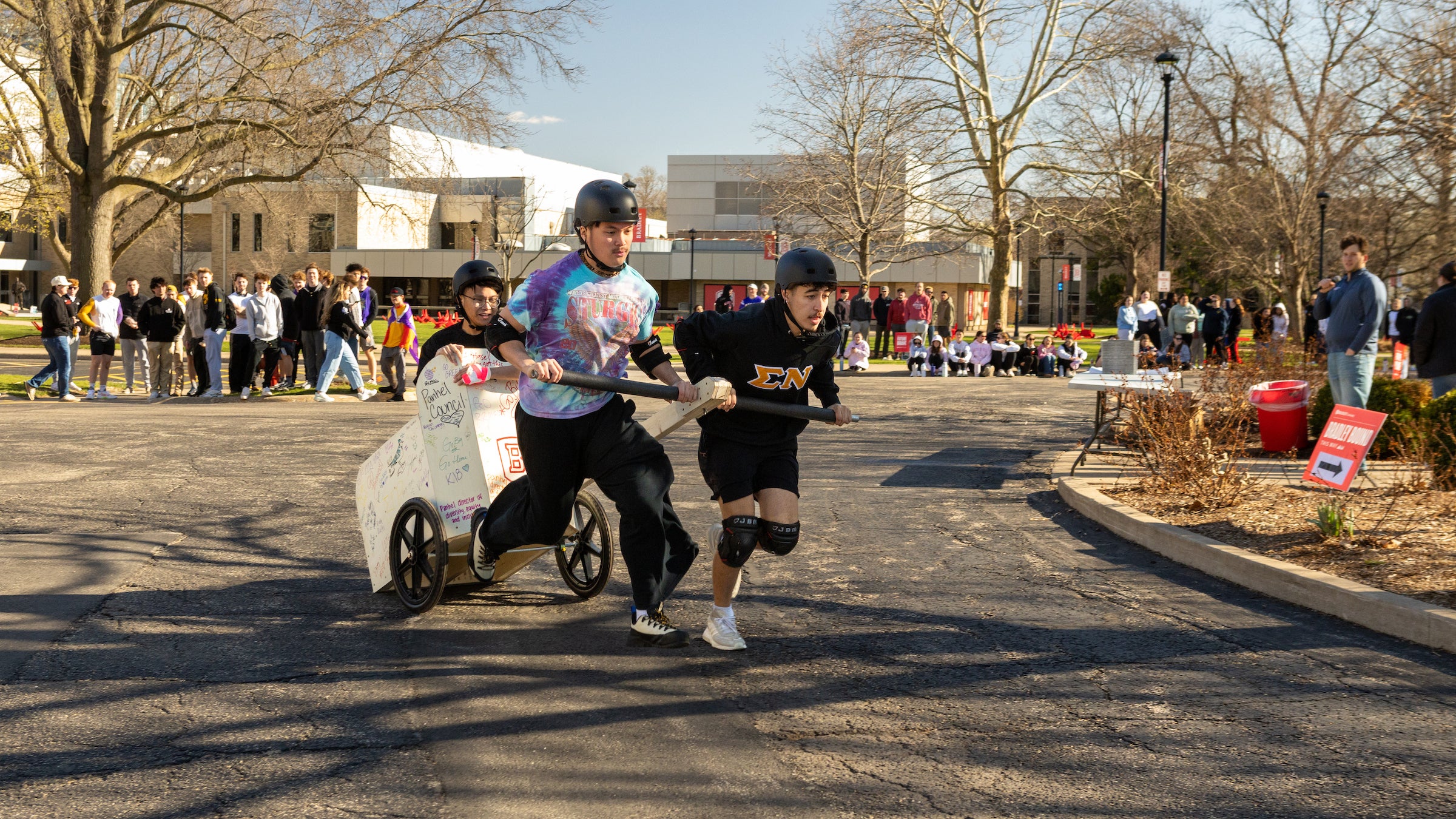 Two students pulling a homemade chariot with a rider