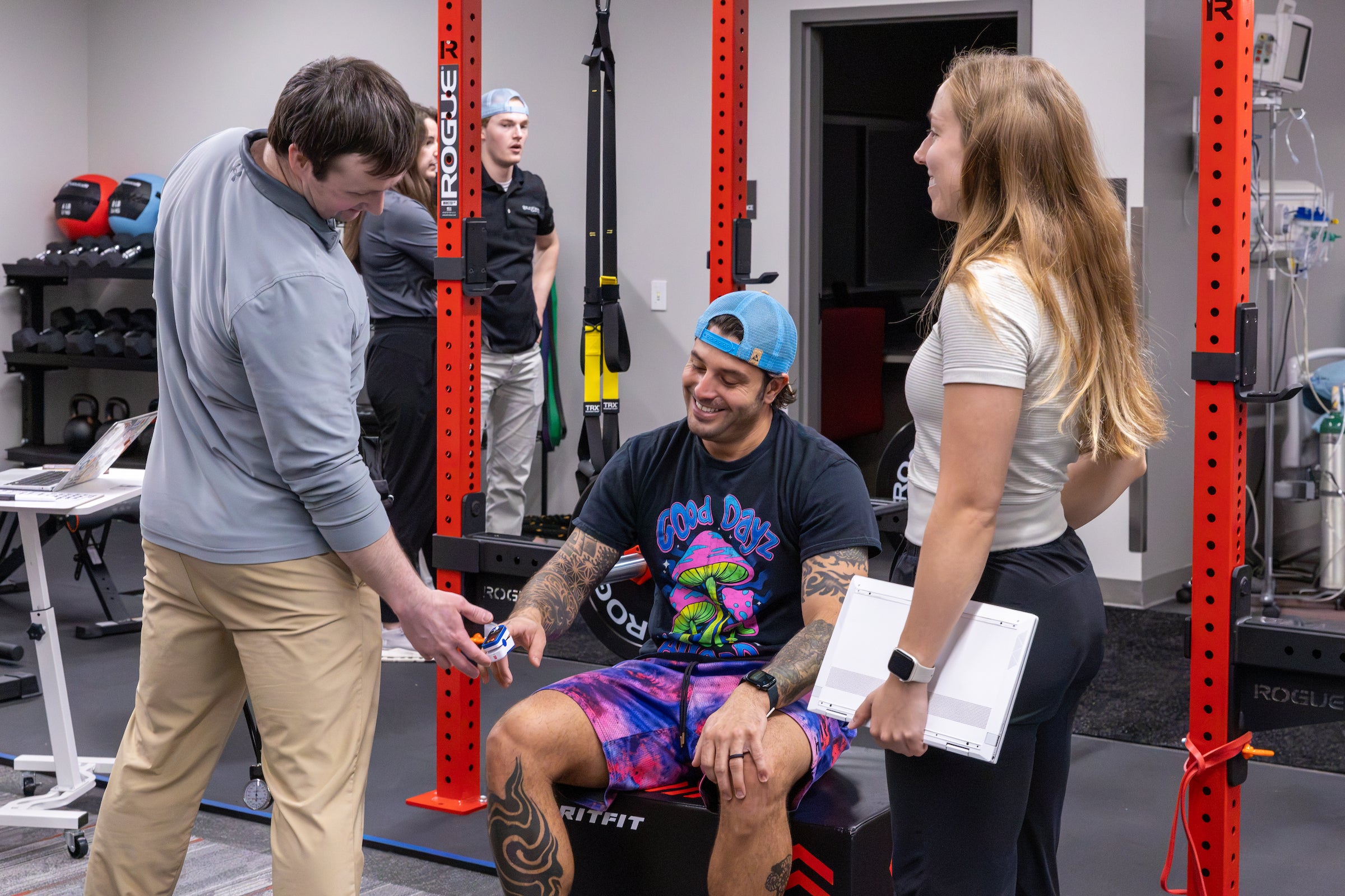 A young man sitting, being coached by a physical trainer in a clinic setting