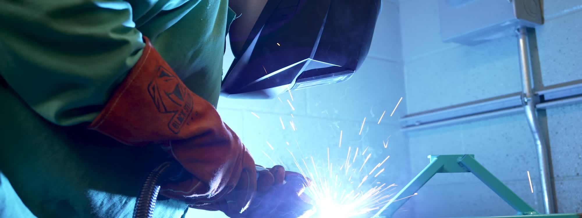 A person in welding gear working with sparks flying