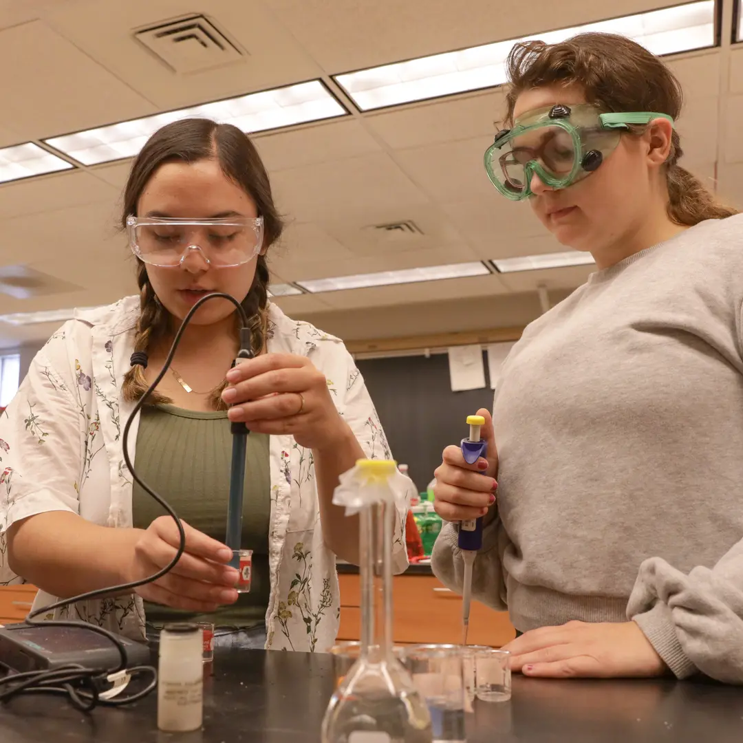 Two students with safety glasses in a lab working with beakers