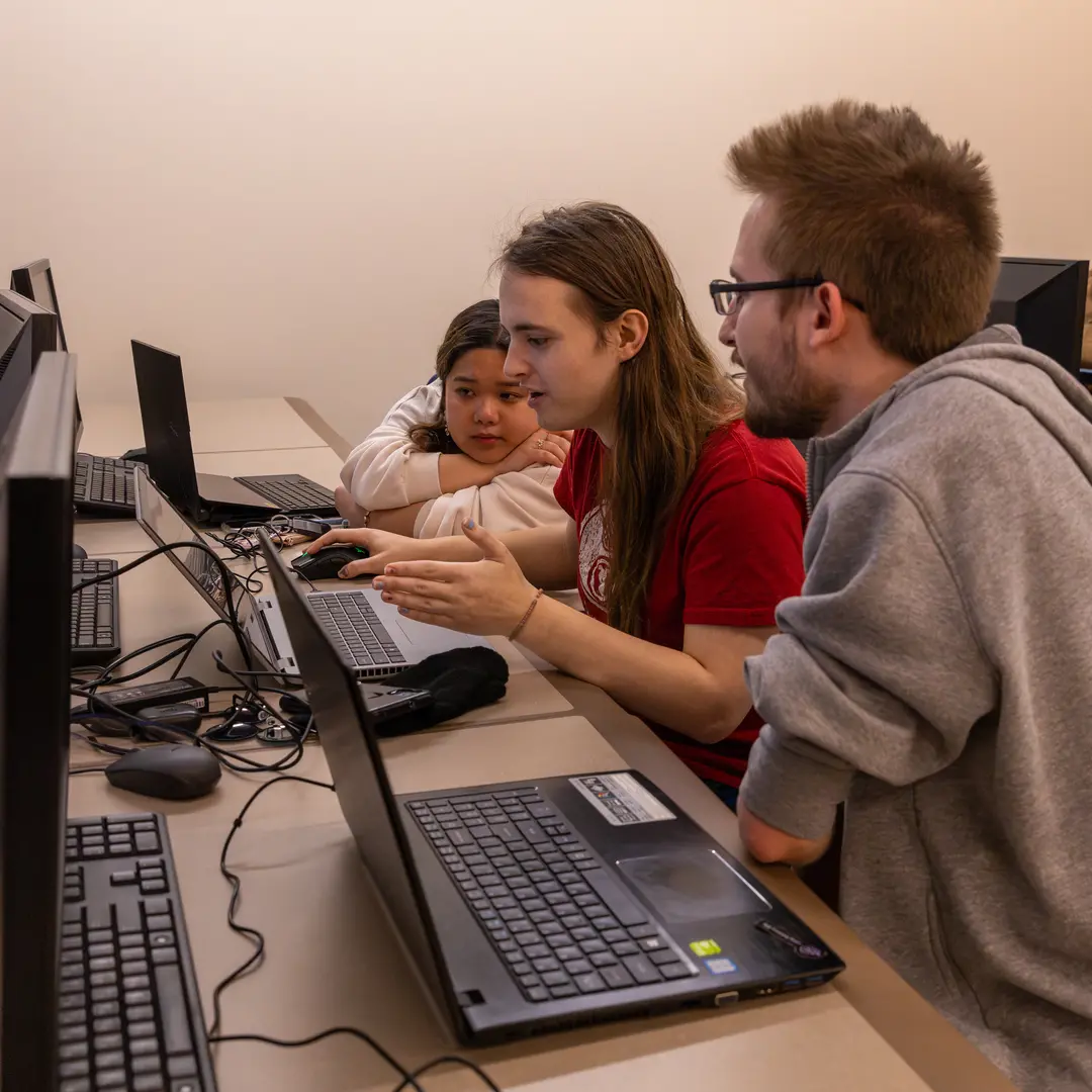 Three students looking at a laptop in the AI computer lab at Bradley