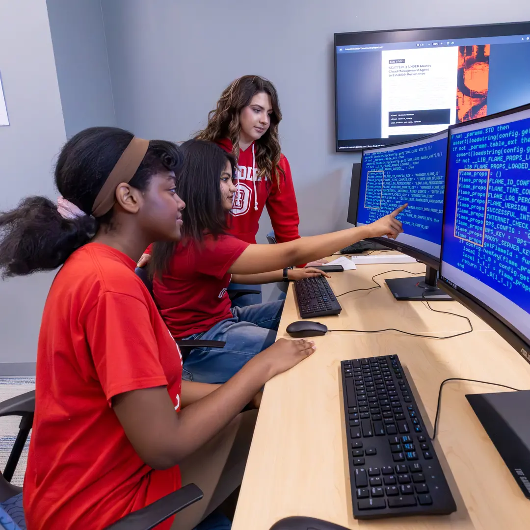 Three female students looking at code on a computer screen