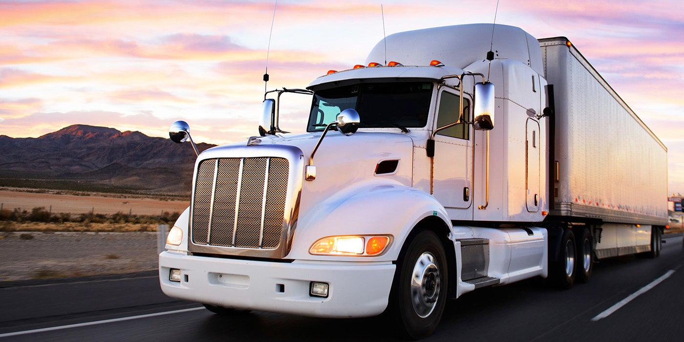 A large freight truck driving down the road at sunset